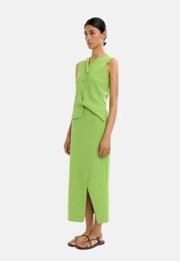 Zielony, dzianinowy top bez rękawów z guzikami z przodu oraz dopasowana długa spódnica z rozcięciem z przodu, uzupełniona brązowymi płaskimi sandałami.