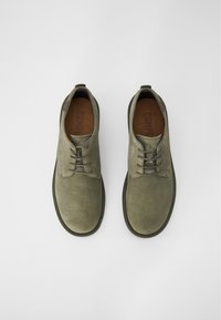 Scarpe in suede grigio con punta rotonda, caratterizzate da un design con lacci e suola in gomma. L'interno presenta una fodera marrone testurizzata.