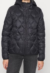 Giubbotto imbottito nero trapuntato con cappuccio, zip frontale e polsini elasticizzati, realizzato in un tessuto leggero e lucido con una trama testurizzata.