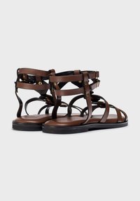 Sandalias gladiador de cuero marrón con múltiples correas, suela plana y acentos en tono dorado. Diseño abierto para mayor transpirabilidad.