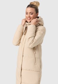 Beige gewatteerde winterjas met een capuchon, vooraan een rits en zijzakken. Gladde textuur met gestikte details en een logov accent op de mouw.