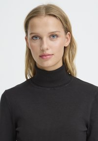 Pull noir à col roulé en tissu fin tricoté. Présente une coupe ajustée et une texture subtile. Style simple et polyvalent sans ornements.