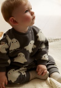 Hall hall beebide dressipluus ja püksid, millel on valged kummituste mustrid naeratavate nägudega, tekst "BABY BOO!" ja soonikkoes mansetid.