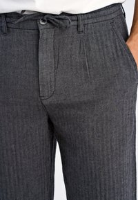 Pantaloni grigi a spina di pesce con vita regolabile con cordoncino, chiusura a bottone e tasche laterali. Il tessuto presenta un delicato motivo a texture.