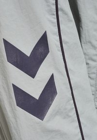 Un tejido gris claro presenta un prominente patrón de chevrón morado y acentos de costura oscura, exhibiendo un diseño elegante y moderno.