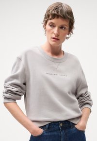 Lys grå sweatshirt med droppede skuldre og ribbede manchetter. Har broderi med teksten "fordi det ikke findes en planet B." Sammen med mørkeblå jeans.