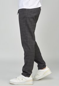 Pantalones a cuadros grises de corte ajustado, confeccionados con una tela texturizada. Usados con zapatillas blancas que cuentan con detalles sutiles y un diseño limpio.