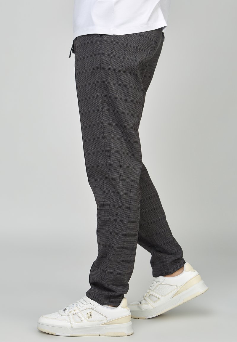 Pantalones a cuadros grises de corte ajustado, confeccionados con una tela texturizada. Usados con zapatillas blancas que cuentan con detalles sutiles y un diseño limpio.