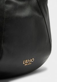Borsa nera in pelle con una superficie testurizzata, caratterizzata da un logo in oro embossato "LIU-JO MILANO" sul davanti.