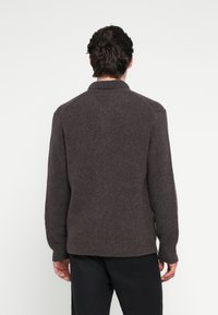 Barna kötött pulóver bordázott szegéllyel és gallérral, puha tapintású és enyhén laza szabású. A hátulnézetben raglán ujjakat mutat.