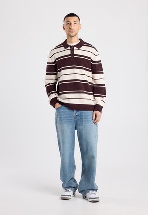 Pull-over rayé crème et bordeaux, doté d'un col et de trois boutons, associé à un jean large bleu clair et des baskets.