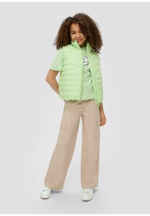 Chaleco acolchado verde claro con cremallera en la parte delantera, combinado con una camiseta verde clara y pantalones cargo de pierna ancha beige. Zapatillas blancas complementan el conjunto.