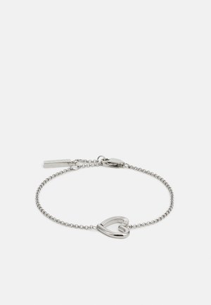 Sølv kjedearmbånd med en stilisert hjertetCharm med ribbet mønster og en hummerlås. Glatt og metallisk finish hele veien.