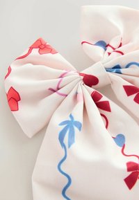 Nœud en tissu léger de couleur crème avec des motifs floraux rouges et bleus. Détail central noué avec des bords en tissu texturé et fluide.