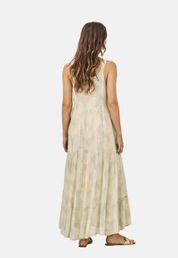 Vestido maxi de tejido ligero con un estampado floral, diseño sin mangas, dobladillo en capas y un corte en la espalda. Los colores incluyen un suave beige y verde.
