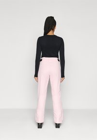 Rosa wasserdichte Skihose mit hohem Bund, Seitentaschen und Reißverschlussbündchen, kombiniert mit einem schwarzen langärmeligen Oberteil.