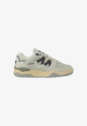 Lichtgrijze Karhu sneaker met beige middenzool, grijze accenten, zwarte veterlussen en een getextureerde rubberen buitenzool, zijaanzicht op witte achtergrond.