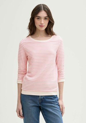 Hellrosa Langarmoberteil mit weißen horizontalen Streifen, runder Halsauschnitt und gerippten Bündchen. Weicher Stoff, kombiniert mit blauen Jeans.