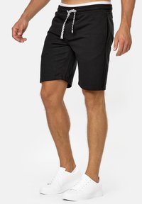 Zwarte sweatshorts met een trekkoord in de taille en twee zijzakken, gemaakt van een zachte stof. Gecombineerd met witte sneakers.