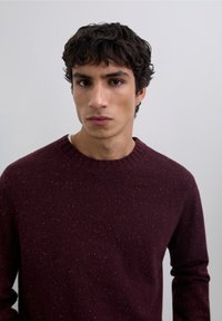 Suéter burdeos de punto confeccionado con tela texturizada, con cuello acanalado y detalles moteados en varios colores.