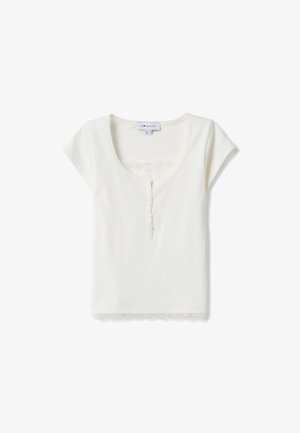 Haut blanc à manches courtes avec encolure arrondie, cinq boutons sur le devant et bordure en dentelle à l'ourlet et à l'encolure, posé à plat sur un fond blanc.
