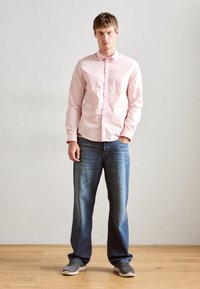 Light pink button-up shirt, relaxed fit blue jeans, gray sneakers. The shirt features a classic collar and subtle texture; jeans are faded.