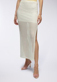 Gonna midi all'uncinetto con un motivo aperto e testurizzato in bianco sporco, caratterizzata da uno spacco alto sul lato sinistro. Abbinata a sandali trasparenti con tacco.