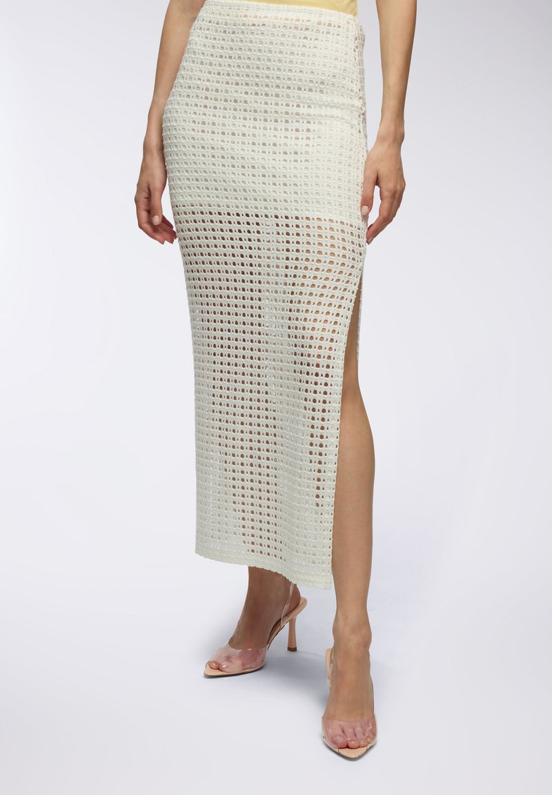 Gonna midi all'uncinetto con un motivo aperto e testurizzato in bianco sporco, caratterizzata da uno spacco alto sul lato sinistro. Abbinata a sandali trasparenti con tacco.