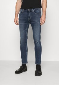 Tajta, mörkblå jeans i denim med en urblekt yta, två framfickor och knäppning med knapp. Matchat med svarta skor.