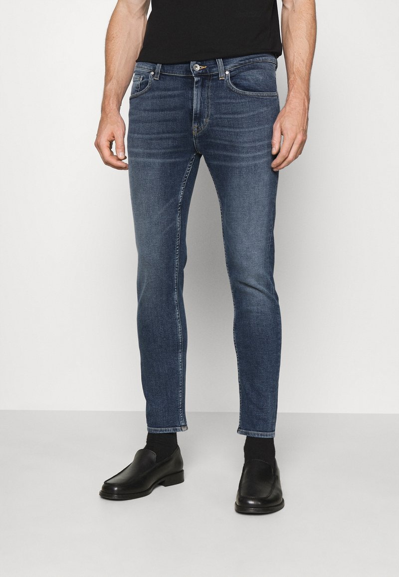 Tajta, mörkblå jeans i denim med en urblekt yta, två framfickor och knäppning med knapp. Matchat med svarta skor.