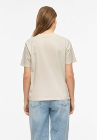 T-shirt bawełniany w kolorze khaki o luźnym kroju, z okrągłym dekoltem i krótkimi rękawami, zestawiony z jasnoniebieskimi jeansami. Gładka faktura, prosty design.