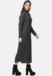 Strickkleid mit langen Ärmeln und Rollkragen in Dunkelgrau, mit Rippstrick-Textur und einem Seitenschlitz. Kombiniert mit schwarzen Plateau-Stiefeletten.