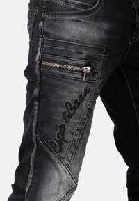 Zwarte denim jeans met een slim fit, ritszak, geborduurd logo en een vervaagde, gestructureerde afwerking langs de benen.