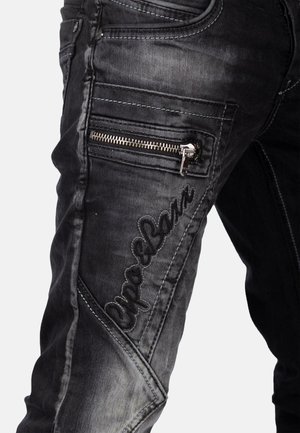 Black denim jeans featuring a slim fit, zippered pocket, embroidered logo, and a faded, textured finish along the legs.