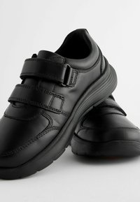 Zapatos de cuero negro con un diseño redondeado. Presentan dobles correas de Velcro, un cuello acolchado, suela texturizada y detalles de costura visibles.