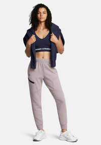 Navy-Sport-BH mit weißem Logo, beige Jogginghosen mit Seitentasche und schwarzen Details, kombiniert mit weißen Sneakers und einem navy Hoodie.