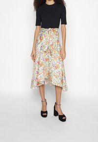 Haut noir à manches courtes associé à une jupe midi fluide ornée d'un motif floral multicolore et d'un détail de taille nouée ; talons plateformes noirs.