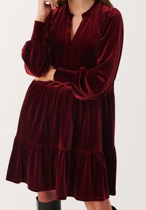 Robe en velours bordeaux avec un ourlet volanté, des manches ballon et un décolleté en trou de serrure ; possède une texture douce et une coupe ample.