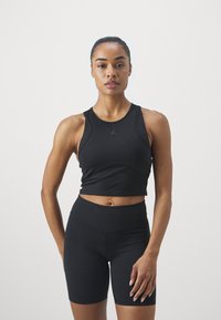 Top deportivo negro de corte crop con un cuello alto y diseño de espalda nadadora, combinado con shorts de ciclismo negros de cintura alta. Tela suave, sin patrones.