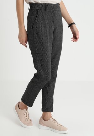 Pantalon noir à motif avec une coupe effilée, doté de poches latérales et accompagné de baskets rose clair, tissu texturé et taille ajustée.