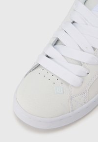 Pantof sport alb cu partea superioară sintetică texturată, șireturi albe, logo mic pe lateral, vârf perforat pentru respirabilitate și talpă din cauciuc.