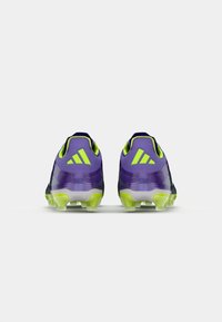 Purple and black soccer cleats with green accents, featuring a textured upper, heel design, and multiple studs on the outsole.