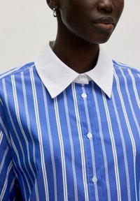 Blau-weiß gestreifte Knopfhemd mit einem weißen Kragen, das eine glatte Stofftextur und dezente Knopfdetails auf der Vorderseite aufweist.