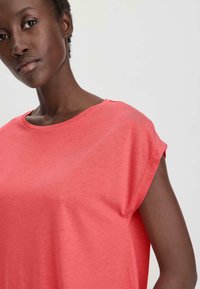 Koraalkleurig t-shirt met een ronde halslijn en korte mouwen. Zacht, soepel materiaal met een iets losse pasvorm en minimale stikseldetails.