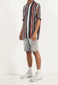 Koszulka w paski z krótkim rękawem w kolorach granatowym, czerwonym i kremowym; w połączeniu z jasnymi, przetartymi szortami jeansowymi. Białe trampki na wysokiej cholewce dopełniają stylizację.