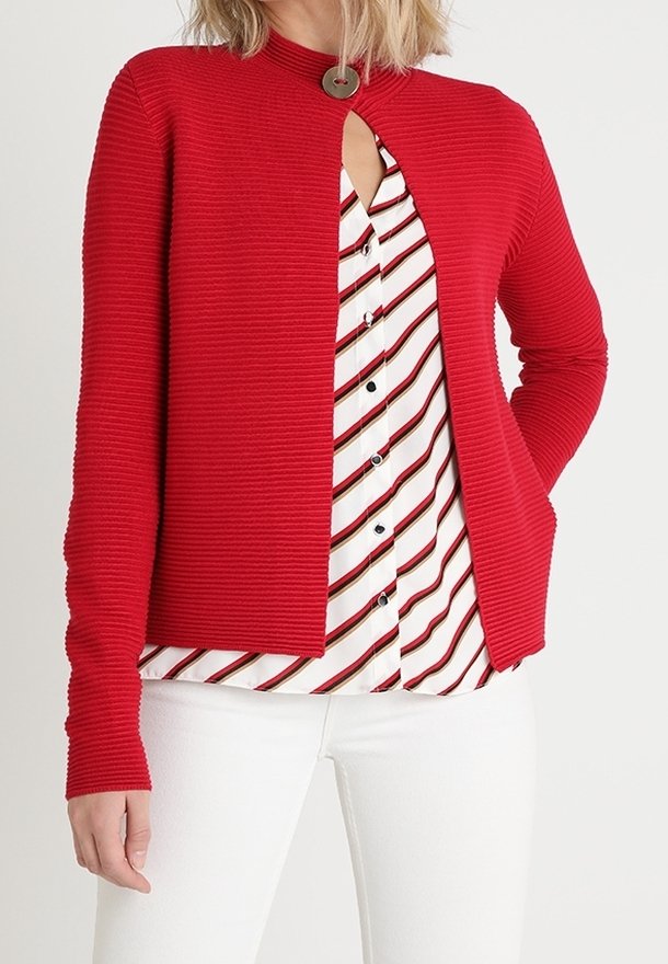 Roter gerippter Cardigan mit hohem Kragen und einer offenen Vorderseite. Getragen über einem weißen Hemd mit roten Streifen. Lange Ärmel und figurbetontes Design.