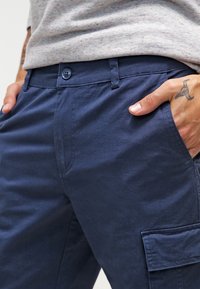 Pantalons cargo bleu marine en tissu léger, dotés d'une fermeture à bouton, de poches latérales et d'une texture subtile.