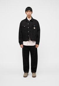 Μαύρο τζιν μπουφάν με κουμπιά και δύο τσέπες στο στήθος, φορεμένο πάνω από ένα ανοιχτό ροζ πουκάμισο. Μαύρο παντελόνι και μπεζ παπούτσια ολοκληρώνουν την εμφάνιση.