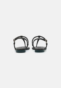 Sorte sorte sandaler i svart skinn med en teksturert såle, tynne stropper og en dekorativ gullspenne ved ankelen. Passer for hverdagsbruk.