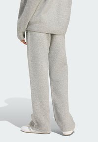 Persona vistiendo pantalones de punto sueltos de color gris claro y suéter a juego con zapatillas blancas, de pie frente a un fondo neutro.